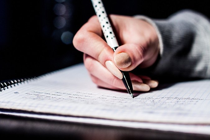 Närbild på en hand och penna tillhörande en student som skriver anteckningar